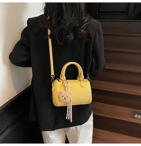 Detail of yellow pebbled leather boston bag with bear charm on model in black suit