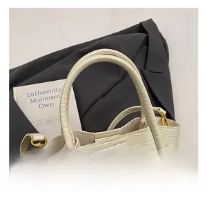 Close-up of cream crocodile pattern handbag with sturdy handles and gold metal hardware