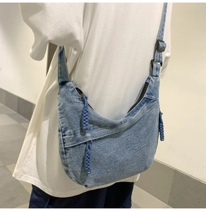 Detail of light blue denim hobo bag featuring black zipper and woven cord puller