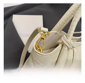 Detailed close-up of gold metal hook fasteners on cream crocodile pattern handbag