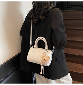 White textured Boston style handbag with plush bear charm on a wooden staircase