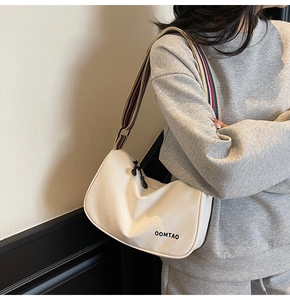 Detail of white moon bag featuring colorful striped wide fabric strap and OOMTAO logo