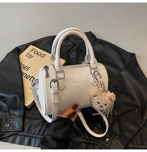 Detailed shot of white lychee leather cylinder bag with teddy bear charm on black jacket