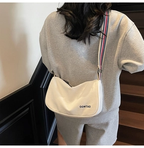 Off-white canvas dumpling bag with striped strap shown in an urban lifestyle scene