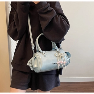 Close-up of light blue barrel handbag with pearl bow charm and adjustable strap detail