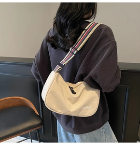 Detail of beige crescent crossbody bag with colorful striped strap on grey sweatshirt
