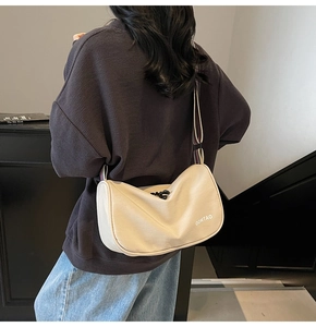 Detail of a creamy white dumpling bag with a colorful striped crossbody strap and logo