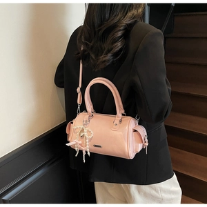 Pink glossy cylinder handbag with pearl bow charm shown as a stylish crossbody bag