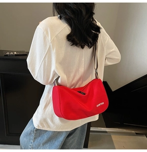 Detail of red canvas crossbody bag with sporty wide striped strap and white lettering