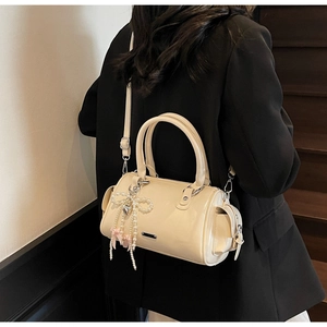 Beige patent leather Boston bag detail with pearl ribbon charm and metallic brand plaque