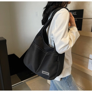 Close-up of black canvas tote bag with white contrast stitching and dual front pockets
