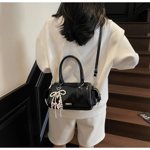 Detail shot of a black glossy Boston bag with pearl bow pendant and crossbody strap