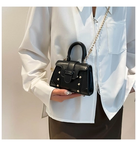 Dettaglio di una mini borsa in pelle nera con borchie dorate e sottile tracolla a catena