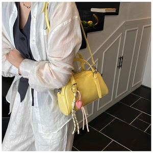 Détail d'un sac bowling jaune vif brillant avec un charme de cœur rose et bandoulière longue