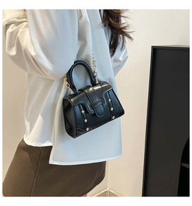 Detail einer schicken schwarzen Ledertasche mit Goldnieten und Metallkettenriemen am Modell