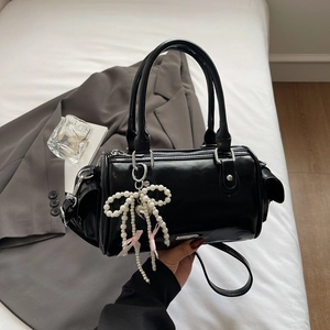Close-up of black patent leather Boston bag with pearl bow and pink ribbon charm