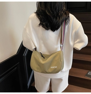 Olive green dumpling crossbody bag with striped wide strap worn on a wooden staircase
