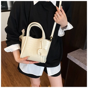 Detail of cream-white crocodile texture bucket bag with cute elephant pendant and gold buckle