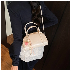 Sac à bandoulière beige élégant porté par un mannequin avec breloque cœur et franges