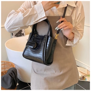 Detail of black crocodile texture mini bucket bag with gold hardware on a leather strap