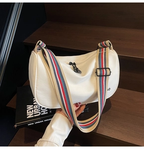 Detail view of white canvas dumpling bag featuring colorful striped wide shoulder strap