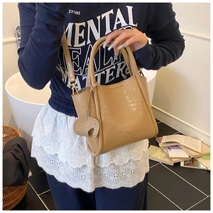 Detailed view of light brown crocodile texture bucket bag with elephant charm and gold strap