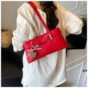 Detail of red pebbled leather underarm bag featuring metal buckles and heart pendant