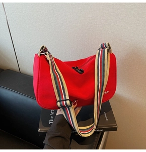 Detail of red nylon dumpling bag with adjustable striped red, blue and beige shoulder strap