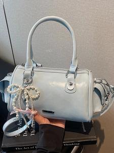 Chic light blue Boston bag with top handles, crossbody strap, and pearl bow detail