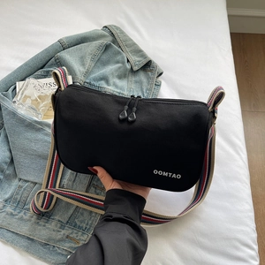 Close-up of black crossbody bag with striped shoulder strap and double zipper detail