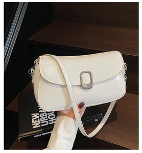Close-up of a white leather crossbody bag with a silver textured buckle on a wooden step