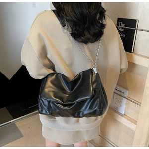 Detail of a large black soft leather crossbody bag with silver chain strap on model
