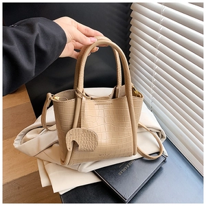 Close-up of beige crocodile pattern bucket bag with elephant charm and shoulder strap