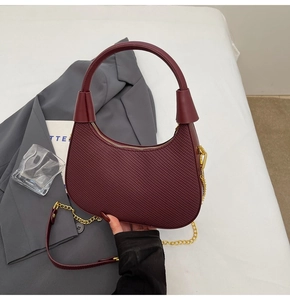 Makroaufnahme einer weinroten Handtasche aus Webleder mit goldener Kettenriemen-Detail
