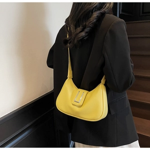 Détail du sac demi-lune en cuir jaune vif porté sur un blazer noir élégant