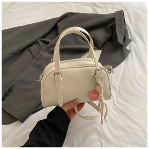 Détail du sac Boston crème avec breloque cœur et bandoulière amovible