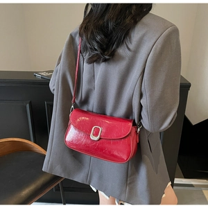 Detail view of red glossy leather shoulder bag with sleek silver buckle on grey blazer