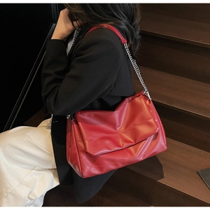Detail of red quilted crossbody bag with silver metal chain strap on black blazer outfit