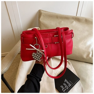 Detail of red lychee textured shoulder bag with heart pendant and silver bow decoration