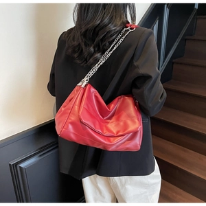 Detail of red quilted hobo bag with silver chain strap worn by a model in a modern interior
