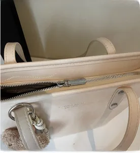Detail of a beige tote bag showing smooth silver zipper and soft plush ball pendant