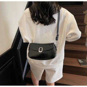Detail of a black patent leather crossbody square bag with silver metal buckle on a model