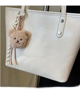 Detail of cream tote bag featuring silver logo, metal rivets, and a plush bear charm