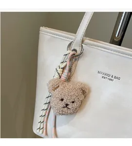 Detail of brown plush bear charm with woven ropes on a white large tote bag