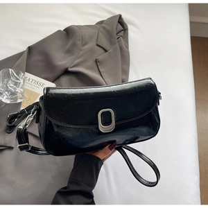 Detail of black glossy faux leather shoulder bag with silver buckle in aesthetic setting