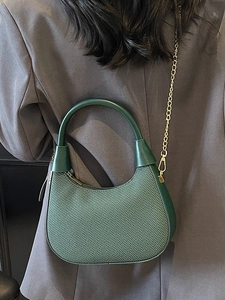 Dunkelgrüne Hobo-Tasche mit strukturiertem Stoff und Goldkette am grauen Blazer