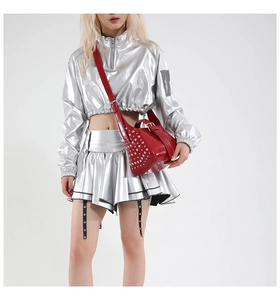 Détail d'un sac à bandoulière rouge clouté avec une tenue mode argentée de style Y2K