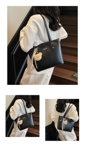 Close-up of black leather tote bag with brand logo and cute teddy bear pendant detail