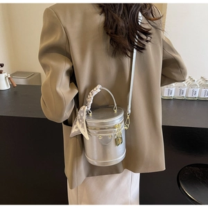 Close-up of a silver cylindrical bucket bag with a silk scarf and metallic charms