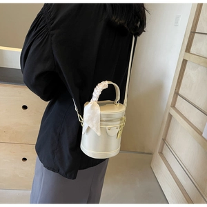 Detail of cream white bucket bag with silk scarf on handle and gold metal hardware